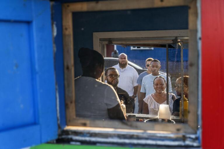 Customers line up to order from Sherica Smith, owner of Shabo's, a popular conch stand in West End, Grand Bahama Island, Bahamas, Sunday, Dec. 4, 2022. While conch can be pricey in the U.S. and elsewhere, it's so ubiquitous in the Bahamas that finding a filling meal of conch for less than $10 is not difficult. That is less than the price of many meats on the island, and conch meat is also found for sale at most grocery stores for eating at home. (AP Photo/David Goldman)