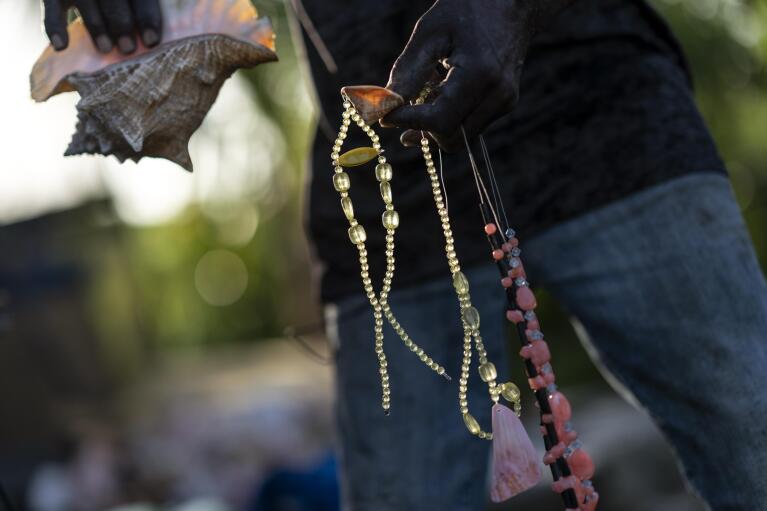 Leroy Glinton holds some of the jewelry he makes from discarded conch shells at his home studio in McLean's Town, Grand Bahama Island, Bahamas, Saturday, Dec. 3, 2022. Glinton's hope is that encouraging more use of conch shells could help reduce fishing pressure on the conch. If fishermen can get more money out of each individual conch by selling or using the shells, they might not need to harvest so many to make a living, he said. (AP Photo/David Goldman)