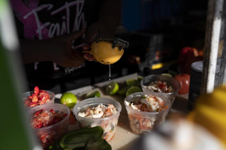 Sherica Smith, owner of Shabo's, a popular conch stand in West End, Grand Bahama Island, Bahamas, squeezes lime onto freshly prepared conch salads Friday Dec. 2, 2022. Smith, who also fishes for conch herself, said she thinks the concern over the disappearance of conch if overhyped. Like many members of the fishery, and many residents of the Bahamas, she thinks fishermen will just need to exert more effort to keep up with demand. (AP Photo/David Goldman)