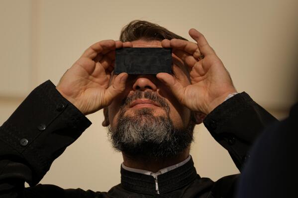 A priest looks through a welding filter during a partial solar eclipse in Bucharest, Romania, Tuesday, Oct. 25, 2022. People around the world gathered Tuesday to witness the last solar eclipse of the year, a phenomenon where the moon briefly casts a black shadow that blocks the sun. It was visible today across Europe, western Asia, northeastern Africa and the Middle East. (AP Photo/Andreea Alexandru)